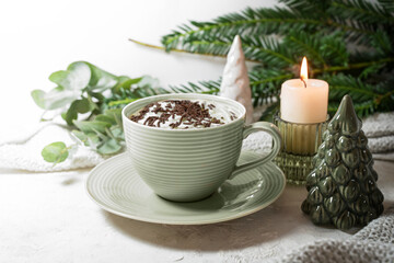 Green cup with hot chocolate and whipped cream, candle, twigs and Christmas decoration on a light background, sweet drink for cozy days at home, copy space, selected focus