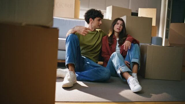 Tired couple moving mortgage talking around cardboard boxes. Family rest floor