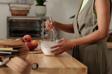 Person whisking batter in modern kitchen, surrounded by fresh ingredients and baking tools. Wooden countertop adds rustic charm to contemporary setting