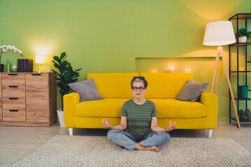Full size photo of lovely senior woman sit floor meditation dressed green outfit home interior room