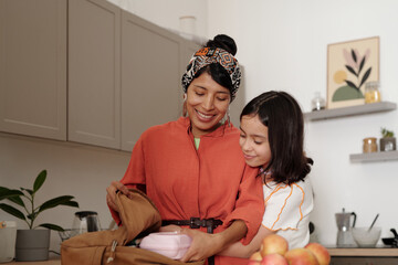 Mother and daughter enjoying time in kitchen, packing lunch in backpack with joy and affection, surrounded by cozy home decor and kitchen essentials