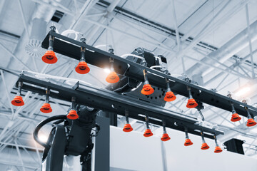 A robot is holding a machine with orange handles. The robot is in a factory setting. The machine is being used to hold a part in place