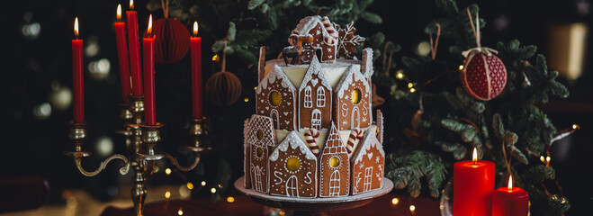 Christmas and New Year beautiful elegant family dinner table setting decorated with candles, fir tree branches. Gorgeous big homemade cake with gingerbread houses as centrepiece. Banner