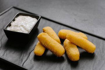 Golden crispy cheese sticks with a creamy dip, served on a sleek black plate. Perfect appetizer