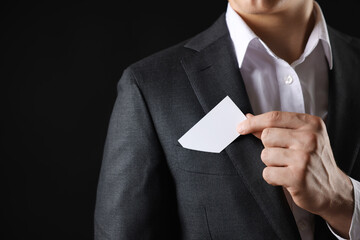 Man taking blank business card from pocket of his jacket on black background, closeup. Mockup for...