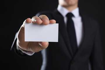 Man holding blank business card on black background, closeup. Mockup for design