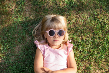 Cute little girl resting on green lawn in park, top view