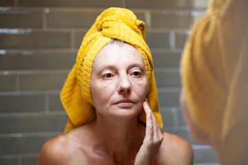 beautiful woman in her forties checking her face in bathroom mirror