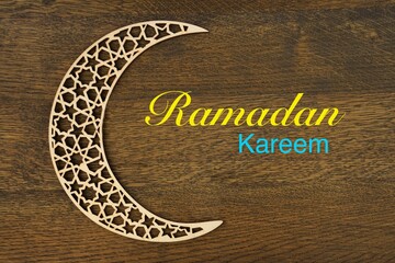 Islamic pattern crescent moon  with "  Ramadan Kareem " text on brown wooden background . 