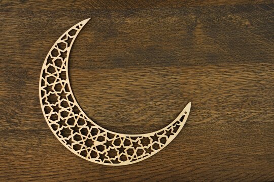 Islamic pattern crescent moon  with laser carved wood on brown wooden background .