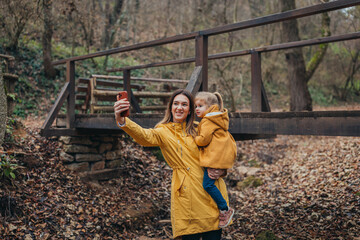 A joyful parent carrying a young child capture a precious moment in a breathtaking forest wearing...