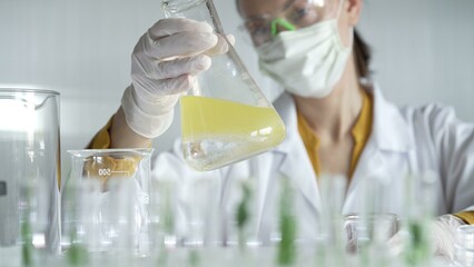 Woman scientist wearing white protective gloves is shaking up a yellow chemical solution inside an...