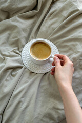 Foto com vista superior de uma mão segurando xícara branca com café, sobre tecido neutro. com espaço livre. espaço para texto. com pessoas.