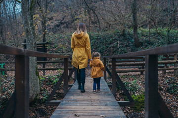 A channeled perspective showing a family journey as a parent and child walk across a wooden bridge amidst a peaceful forest, emphasizing nature’s embrace and security.