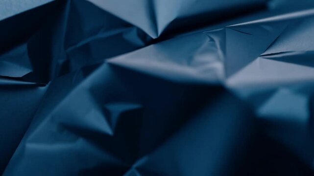 The crumpled dark blue paper exhibits intricate creases and folds, creating an abstract textural backdrop ideal for artistic or design purposes.