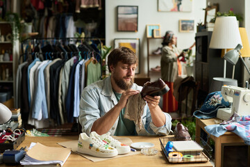 Bearded male owner of modern thrift shop wiping brown secondhand boots with duster while upcycling them