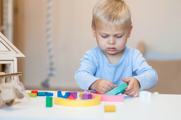 A little boy of 2 years old is playing a developing logistics constructor. Children's wooden toys. Montessori for child development.