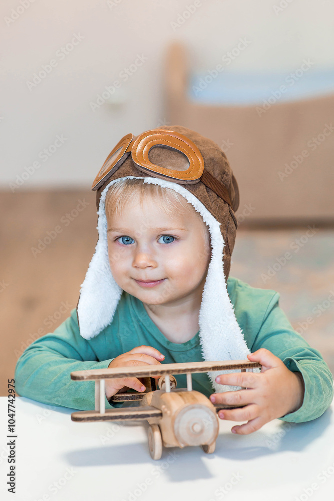 Wall mural a handsome little boy of 2 years old in a pilot's hat is playing with a wooden airplane and a logist