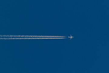 jetliner crossing the cloudless blue sky leaving a vapor trail.