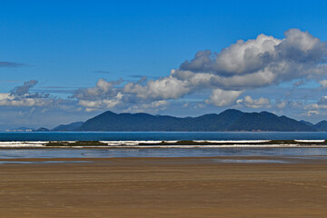 wide strip of sand during low tide, in the background a calm sea and cumulus clouds over the mountains of Serra do Mar