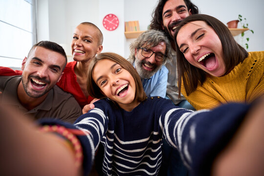 Cheerful Caucasian family taking selfie photo with funny expressions at home. Multi-generational happy diverse people looking joyful at front camera at living room indoor. Positive domestic relations
