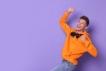 Happy young student with headphones on violet background, space for text