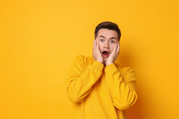 Portrait of scared young man on orange background, space for text