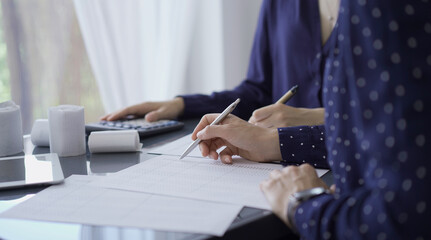 Two unrecognizable female accountants or auditors are sitting and reviewing financial documents in office. Audit and taxes