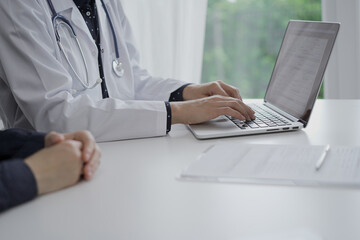Doctor and a patient in clinic. The female physician is using laptop computer for filling up medication history record form, close up. Medicine and science