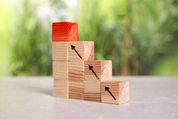 Stair made of wooden blocks on table. Cubes with arrows showing way to red one. Steps to success...