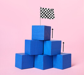Pyramid made of blue cubes with finish flag on top against pink background. Arrows showing way to...