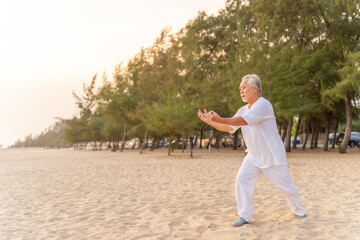 Asian senior man enjoy outdoor lifestyle travel nature ocean on summer holiday vacation. Elderly man do relaxing exercise tai chi, yoga on the beach at sunset. Wellness, health care motivation concept