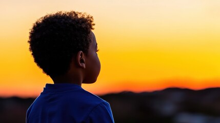 A child with curly hair gazes at a vivid orange sunset sky, embodying the wonder and innocence of youth in a serene outdoor setting, silhouetted beautifully.