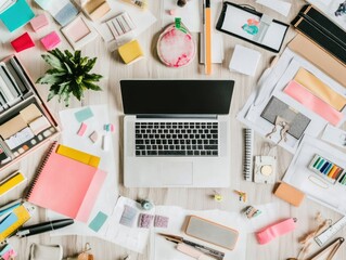A cluttered workspace with a laptop, sticky notes, stationery, and a small plant.