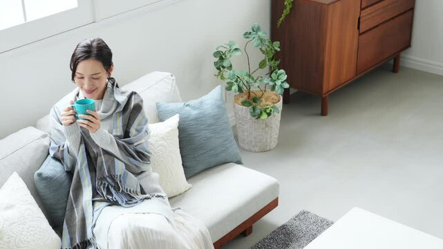 寒い、冬、暖かい、コーヒー、笑顔、女性、日本人、暖冬、対策、防寒、ストール、ショール、ブランケット、コピースペース、インテリア、リビングルーム、ライフスタイル、おしゃれ、リラックス、ほっこり、安心、ソファー、若い、寒暖差、紅茶、カップ、飲む、暖房、エアコン、マフラー、ポジティブ、快適、節電、室内、明るい、省エネ、爽やか、毛布、シンプル、キレイめ、きれいめ、セーター、ニット、寒さ、寒気、冷気、住宅、