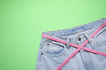 Jeans and measuring tape on green background, top view. Space for text