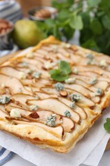 Delicious puff pastry tart with pears, almond, mint and blue cheese on white table, closeup