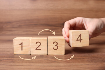 Man putting cube with digit 4 to row of other numbered ones onto wooden table, closeup....