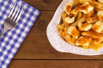 Poutine plate on a wooden background. Cooked with french fries, gravy and curd cheese. Canadian cuisine.