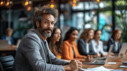 Diverse business team collaborating with laptops and tablets in a meeting room with male manager presenting to female colleagues at conference table discussing project