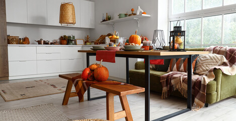 Interior of modern kitchen with served dining table, pumpkins, bench and sofa