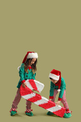 Cute little children in elf's costumes and with Christmas pinata on green background