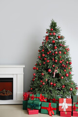 Christmas tree with ornaments, gift boxes and fireplace near white wall