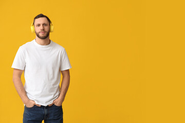 Young man in modern headphones on yellow background