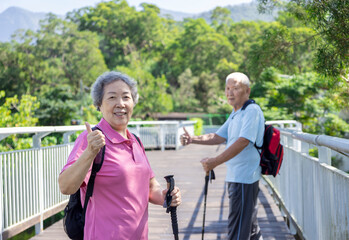 Happy asian senior couple hiking in the nature and showing thumbs up