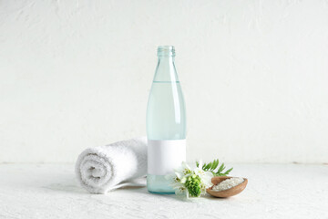 Bottle of natural rice water, grains, clean towel and flower on light background