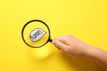 Woman magnifying speech bubble with word RUMORS on yellow background. Gossip concept