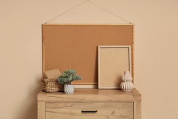 Vase, houseplant, basket and frames on chest of drawers near beige wall. Closeup