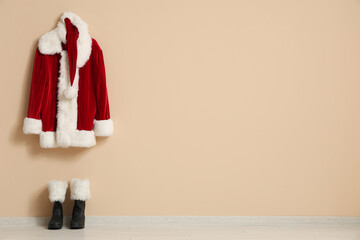 Hanger with Santa Claus costume and boots near beige wall in room