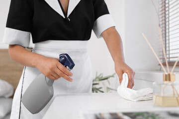 Young chambermaid cleaning furniture in hotel room, closeup